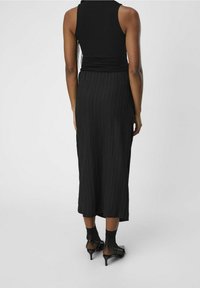 Robe noire côtelée avec un haut ajusté à encolure dégagée et une jupe fluides jusqu'aux chevilles. Portée avec des talons noirs à fines lanières.