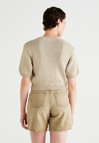 Μπεζ πλεχτό πουλόβερ με κοντά φουσκωτά μανίκια, ριχτό στρίφωμα, συνδυασμένο με μπεζ τζιν σορτς με πίσω τσέπες και υφή.