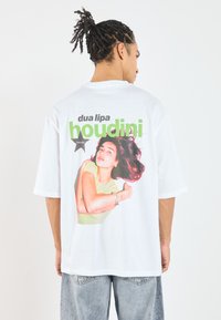 Hvit oversized t-skjorte med et fargerikt grafisk trykk av en kvinne, med teksten "dua lipa" og "houdini" fremtredende.