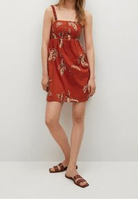 Rotes ärmelloses Kleid mit Blumenmuster, taillierter Oberteil und ausgestellt Rock. Kombiniert mit braunen flachen Sandalen. Glattes Material, lässiges Design.