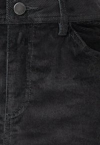 Schwarzer Cordstoff mit ausgeprägten vertikalen Rippen und einer glatten Textur. Enthält eine Fronttasche und ein Metallknopf-Detail.