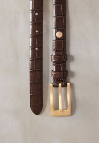 Brunt bälte i krokodilpräglat läder med spänne i guldfärgad metall, med dekorativa detaljer och flera justeringshål.