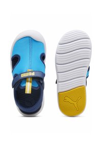 Blå och marinblå sportskor med kardborreband, texturerad sula och Puma-logotyp. Lättviktig design som är perfekt för vardagsbruk.