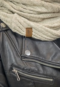 Sort lædermotorcykeljakke med sølvhardware og lynlåse, parret med et cremet strikhalstørklæde, der viser et tekstureret mønster og et lædermærke.