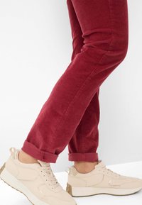 Rode corduroy broek met opgerolde broekspijpen, gecombineerd met beige sneakers met een gestructureerde bovenkant, gladde accenten en een dikke zool.