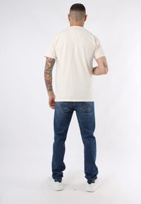 T-shirt in cotone beige chiaro, maniche corte, colletto a girocollo, abbinato a jeans in denim blu scuro, con una leggera scoloritura e tasche posteriori.