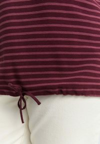 Haut rayé bordeaux avec un ourlet à cordon. Tissu doux et texturé avec des accents violets. Associez-le à un bas blanc pour le contraste.