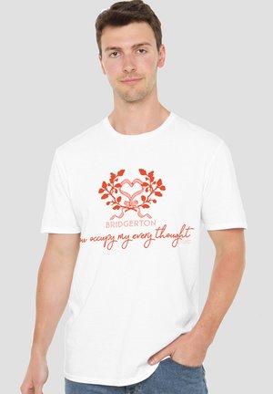 Young man wearing a white T-shirt with a red heart-shaped floral design and the text "BRIDGERTON you occupy my every thought."