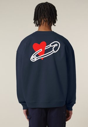 Marineblauwe sweatshirt met een groot wit en rood hart en een veiligheidsspeldontwerp op de achterkant. Gemaakt van zachte stof met geribde boorden.