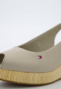 Chaussure beige compensée à bout ouvert, semelle plateforme texturée tissée et petit logo rectangulaire rouge, blanc et bleu sur le côté supérieur.
