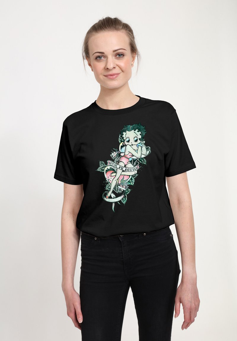 Sort t-shirt med et farverigt grafik af en karakter med grønt hår og lyserøde klæder, omgivet af blomstrelementer og et banner.