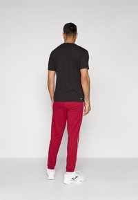 Black short-sleeve t-shirt paired with red sweatpants featuring white side stripes. The individual wears white sneakers.