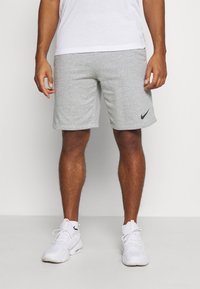 Man som bär vita sneakers, vita strumpor, grå Nike-shorts och en vit t-shirt står mot en enkel bakgrund.