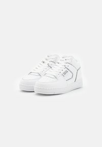 White high-top sneakers with perforated detailing, flat laces, and a textured sole. Features a contrasting logo patch on the side.