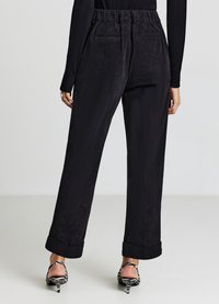 Schwarze Cordhose mit weitem Bein und hohem elastischem Bund, ausgestattet mit zwei Gesäßtaschen und umgeschlagenen Säumen, kombiniert mit zebra-gestreiften High Heels.