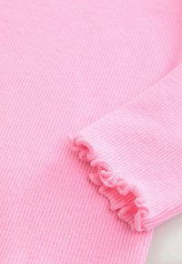 Material roz cu reilități, cu un finisaj texturat, având detalii cu manșete cu volane. Materialul este moale și ușor, creând o margine ondulată.