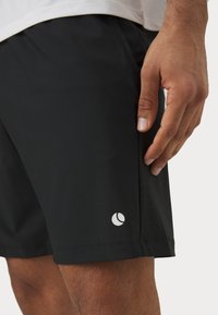 Calções atléticos pretos feitos de material leve, apresentando um logótipo branco na bainha e detalhes texturizados ao longo do lado.