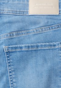Pantalones vaqueros de mezclilla azul claro con bolsillo trasero con doble costura y una etiqueta beige que dice "Street One - Denim ALL TIME FAVOURITE" en la cintura.