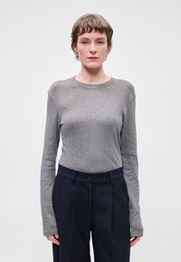 Camisola cinza de manga longa com decote redondo, feita de tecido suave, combinada com calças azul-marinho com riscas verticais e dois botões.