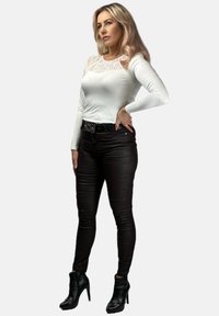 Biała bluzka z długim rękawem z koronkowymi detalami przy dekolcie, w połączeniu z dopasowanymi czarnymi spodniami skórzanymi i czarnymi botkami na obcasie.