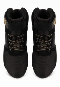 Melni augstie trenažieri, kas izgatavoti no kanvas un zamšādas, ar zelta akcentiem, teksturētu apdari un šņorēm, kas nodrošina mīkstāku potīšu atbalstu.