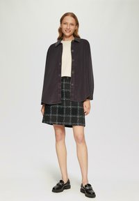 Veste chemise oversized en velours côtelé gris avec des boutons, haut crème, jupe à carreaux noirs et mocassins noirs. Textures lisses et design structuré.