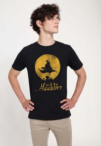Czarna bawełniana koszulka z żółtą grafiką przedstawiającą Aladyna i latający dywan, z napisem "Aladyn" w ozdobnej czcionce poniżej.