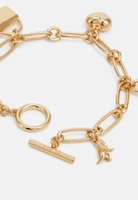 Gold chain bracelet featuring oval and round links, a toggle bar, and a decorative charm shaped like a dinosaur. Smooth, shiny texture.
