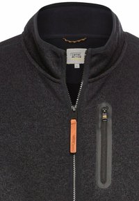 Donkergrijze fleece jack met rits en hoge kraag. Voorzien van een leren ritsen trekker en een ritszak op de borst met een zwart accent.