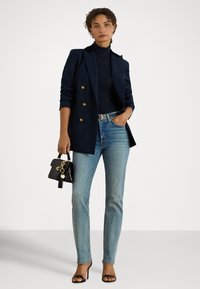 Tumši zils dubultpogu žakete, pieguļošs augsts apkakls, gaiši zilas džinsa bikses, melna mini soma ar zelta akcentiem un melnas siksnainas augstpapēžu sandales.