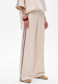 Beige wijde broek met verticale bordeauxrode en zwarte strepen. Zachte stof met een relaxed fit, gecombineerd met een losse beige top.