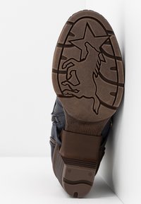 Suela de un zapato marrón con un patrón de caballo y estrella grabado en la parte inferior, apoyada sobre una superficie blanca.