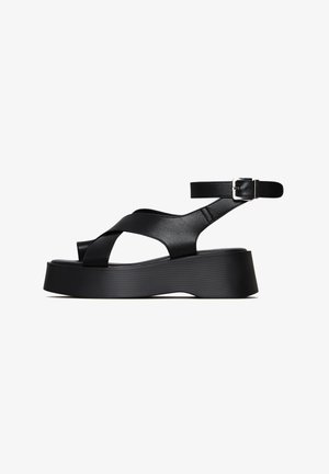 Sandali platform neri con cinturini incrociati e fibbia alla caviglia. Realizzati in pelle liscia con suola testurizzata e forma sagomata.