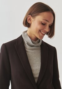 Gray ribbed turtleneck under a dark blazer. The blazer features a tailored fit with sharp lapels. Smooth textures and neutral color palette.