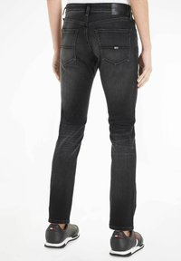 Jeans de mezclilla negros con corte ajustado, que cuentan con bolsillos traseros y costuras discretas. Combinados con zapatillas deportivas grises, mostrando un aspecto casual.