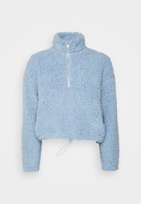 Blå fleecetröja med hög krage, halvdragkedja, kort längd och dragsko i nederkant. Mjuk, texturerad yta, långa ärmar.