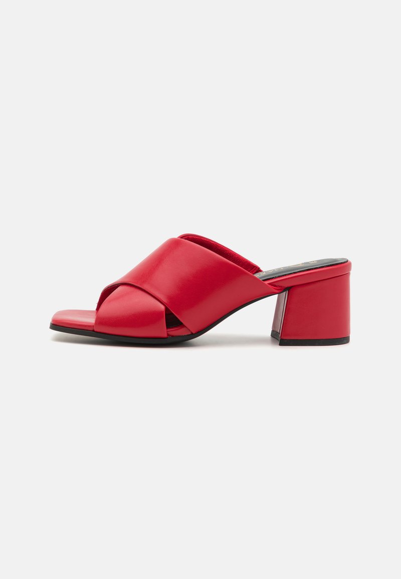 Mules en cuir rouge à talons carrés avec un design à bout ouvert, présentant une sangle croisée et une texture lisse. Hauteur du talon d'environ 5 cm.