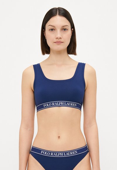 Granatowy stanik sportowy i dopasowane bikini, z kwadratowym dekoltem i białą elastyczną taśmą z logo. Gładka, prążkowana tekstura.