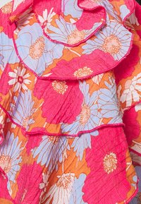 Buntes, blumenmusterndes Stoff mit geschichteten Rüschchen. Enthält rosa, orange und hellblaue Blumen mit einer strukturierten, zerknitterten Oberfläche.