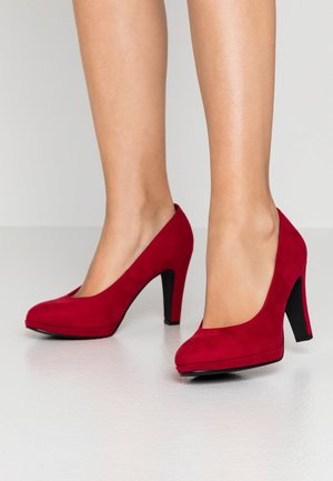 Des chaussures à talons hauts en rouge en suede avec un bout rond et une texture lisse, dotées d'un talon et d'une plateforme noire pour ajouter de la hauteur.
