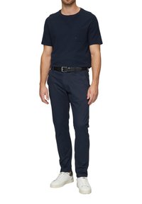 Donkerblauwe katoenen T-shirt met een borstzak, gecombineerd met donkerblauwe broek, een zwarte riem en witte sneakers; eenvoudig ontwerp en casual pasvorm.