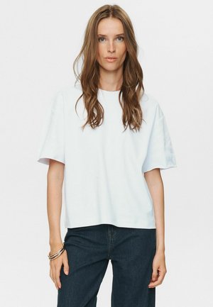 White short-sleeve t-shirt with a relaxed fit, round neckline, and smooth cotton texture. Paired with dark blue denim jeans.
