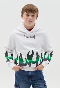 Witte hoodie met een vlamontwerp in zwart en groen op de mouwen en onderkant, met het woord "Fearless" in paars gedrukt op de borst.