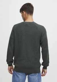 Pulover tricotat verde închis cu textură ribbată, guler rotund și mâneci lungi. Are o croială lejeră și este de culoare solidă, fără modele.