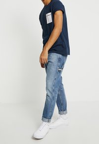 Námořnické tričko s bílou kapsou a textem, doplněné o světle modré tapered džíny a bílé tenisky. Ležérní střih s ohrnutými manžetami.