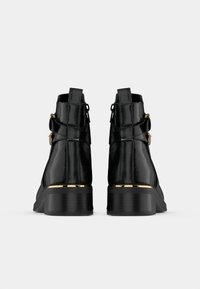 Čierne členkové topánky s lesklým povrchom, s textúrovaným zvrškom, zlatými akcentmi na päte a zadnými úchytkami pre jednoduché obúvanie.