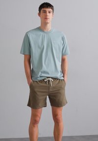 Lichtblauwe katoenen t-shirt met een ronde halslijn en korte mouwen, gecombineerd met bruine shorts met een trekkoord in de taille en zijzakken.