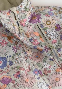 Dziecięca kurtka w kwiatowy wzór z zamkiem błyskawicznym i zatrzaskami, zdobiona pastelowymi kwiatami, motylami oraz małymi ilustracjami zwierząt.