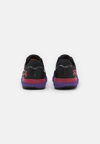 Une paire de chaussures de sport noires, violettes et rouges vue de l'arrière avec le logo Under Armour sur le talon, isolée sur un fond blanc.