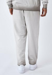 Lichtgrijze joggingbroek gemaakt van zachte stof, met een ontspannen pasvorm, elastische tailleband en boorden, gecombineerd met witte sneakers.